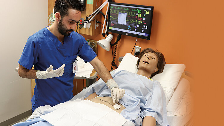 Un étudiant dans un chambre d'hôpital ajuste les points de suture sur le ventre d'un mannequin intelligent.