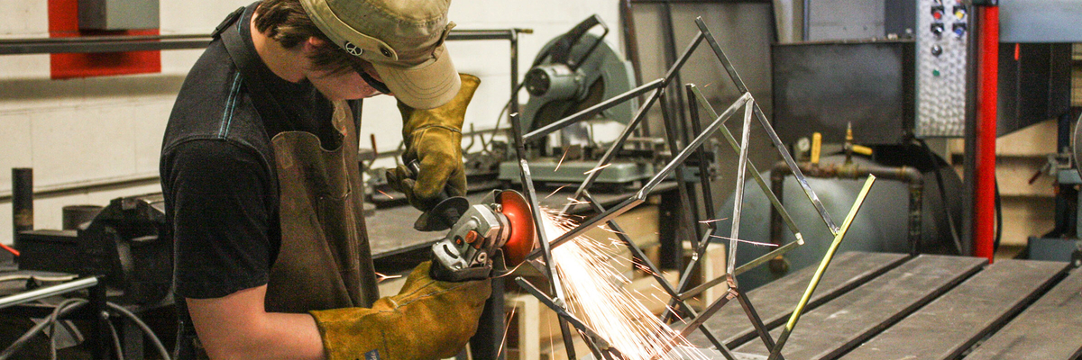 Un étudiant avec une scie travaille sa sculpture en atelier.