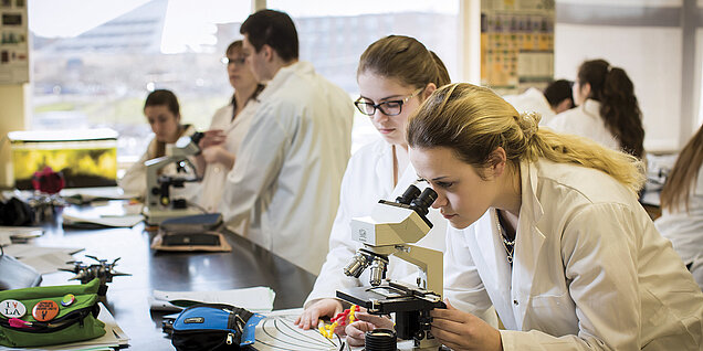 Une étudiante regarde dans un microscope.
