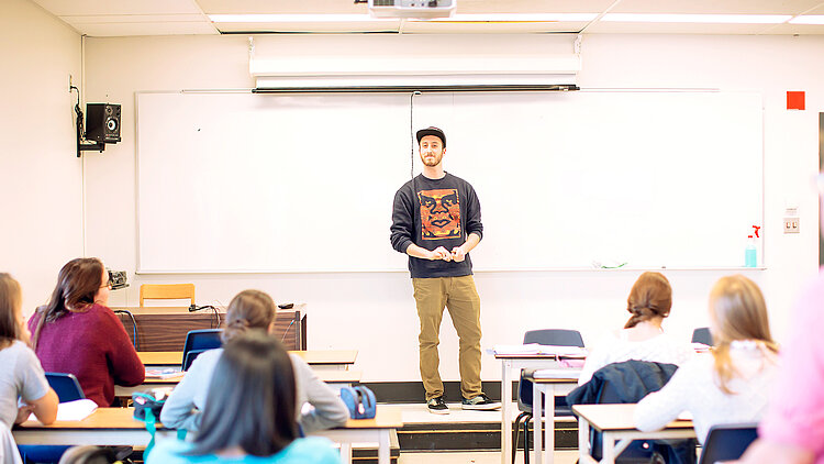 Un étudiant fait une présentation devant ses camarades en classe.