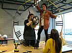 Des étudiantes debout sur une table en classe montent une horloge géante.