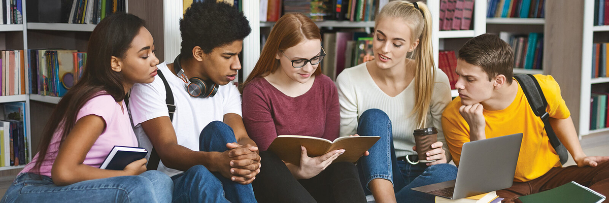 Cinq étudiants assis par terre dans une bibliothèque observent un livre.