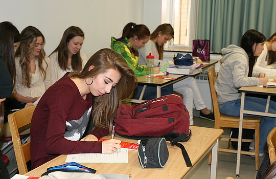 Une étudiante prend des notes à son pupitre.