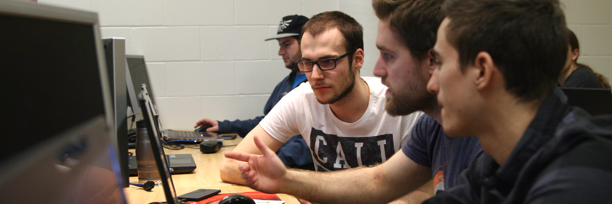 Trois étudiants discutent en regardant un écran d'ordinateur.