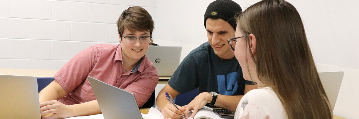 Trois étudiants prennent des notes à table avec leur ordinateur portable.