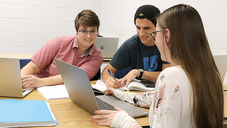 Trois étudiants prennent des notes à table avec leur ordinateur portable.