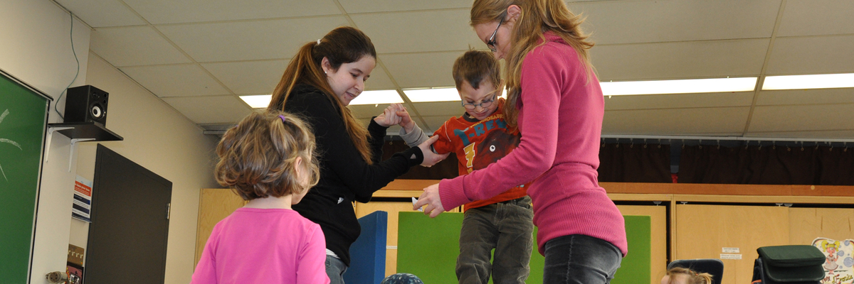 Des étudiantes aident un petit garçon à grimper sur une glissade, en classe.