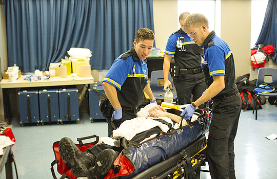 Des étudiants s'apprêtent à soulever un patient sur une civière.
