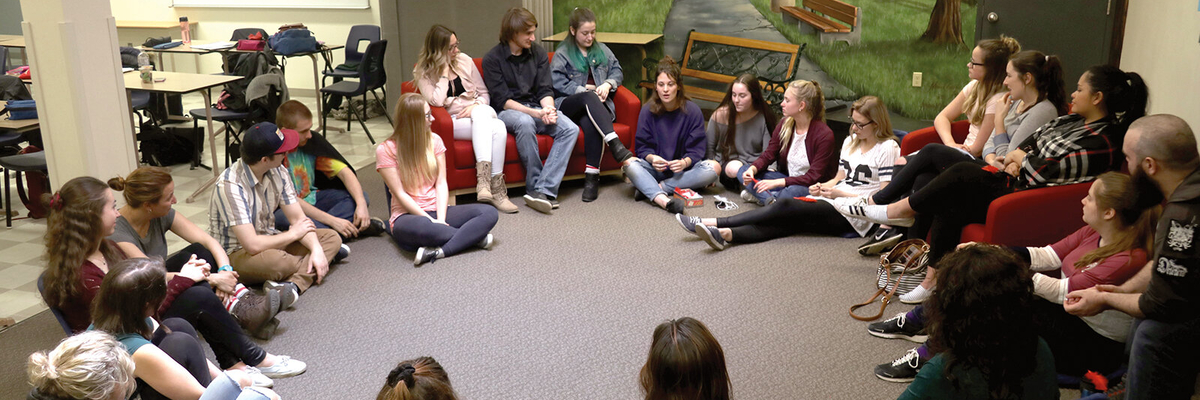 Un grand groupe d'étudiants discute en cercle dans une salle de cours.