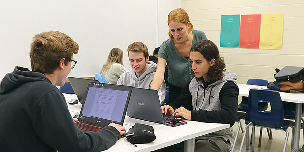 Une professeure donne une explication à des étudiants qui sont assis à leur bureau avec un portable.