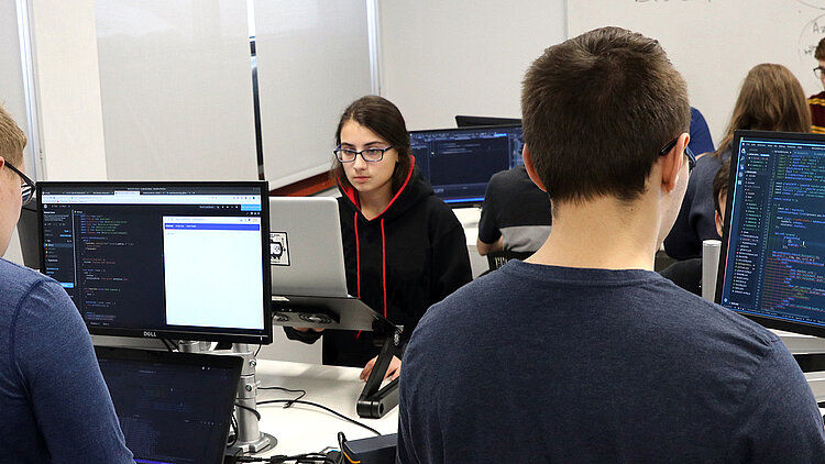 Une étudiante et deux étudiants programment sur un ordinateur.