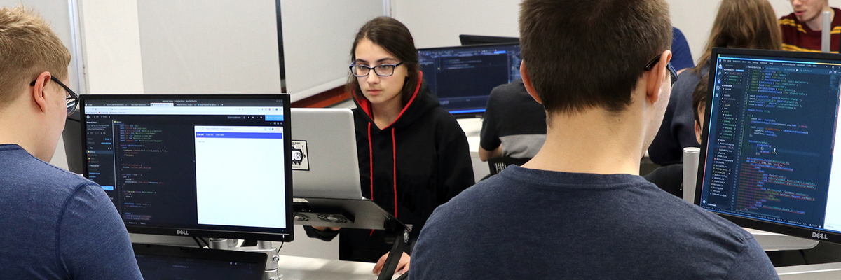 Une étudiante et deux étudiants programment sur un ordinateur.